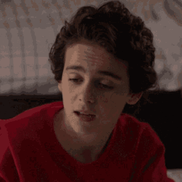 a young boy wearing a red shirt is sitting on a bed with his eyes closed