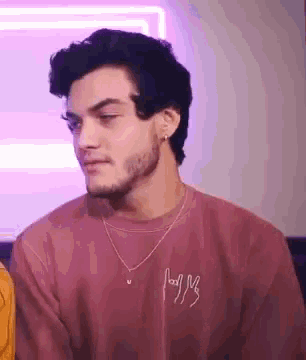 a man with a beard is wearing a pink sweater and a necklace while sitting on a couch .