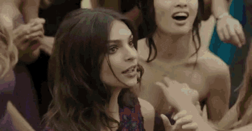 a woman in a purple dress is standing in a crowd of people and pointing at something .