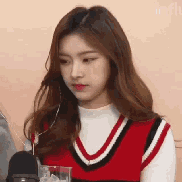 a young woman is sitting in front of a microphone wearing a red vest and headphones .
