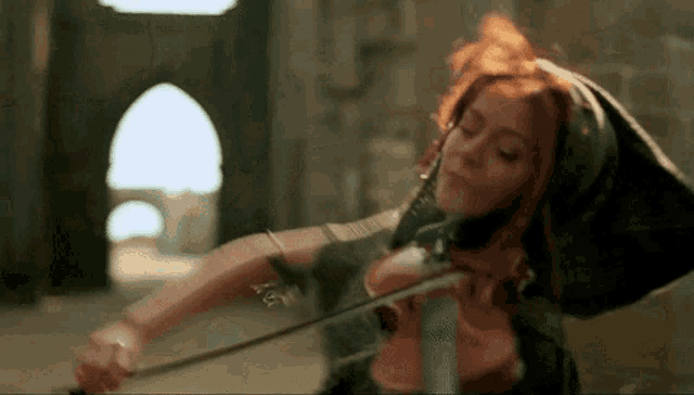 a woman with red hair plays a violin in front of a stone wall