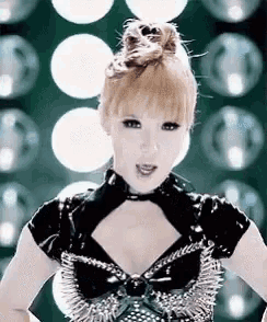 a woman is standing in front of a wall of lights wearing a black top with spikes on it .