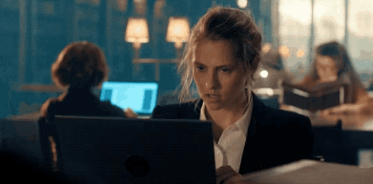 a woman in a suit sits at a table using a laptop