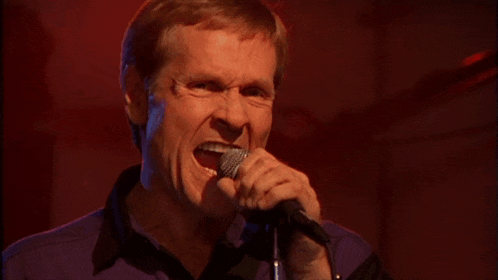 a man sings into a microphone with his mouth wide open