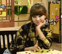a woman is sitting at a table with her hand on her chin and playing a game of go .