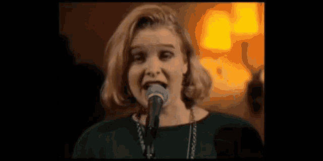 a woman is singing into a microphone while wearing a green shirt .
