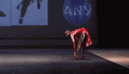 a woman in a red dress and red gloves is dancing on a runway .