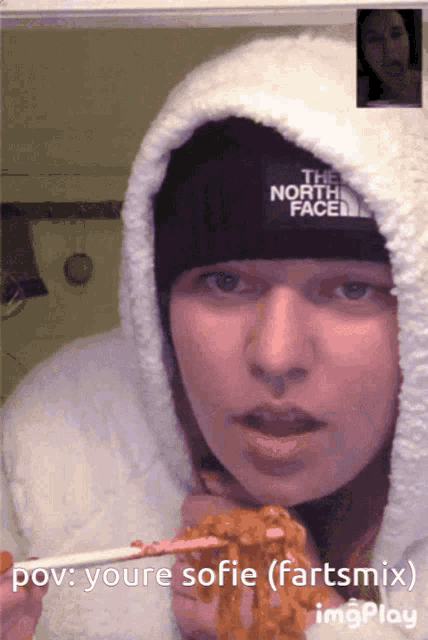 a woman wearing a north face hat eating noodles with chopsticks