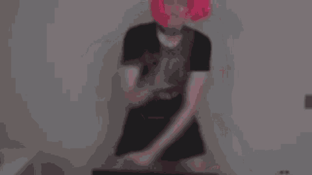 a man wearing a pink wig and a black t-shirt is dancing .