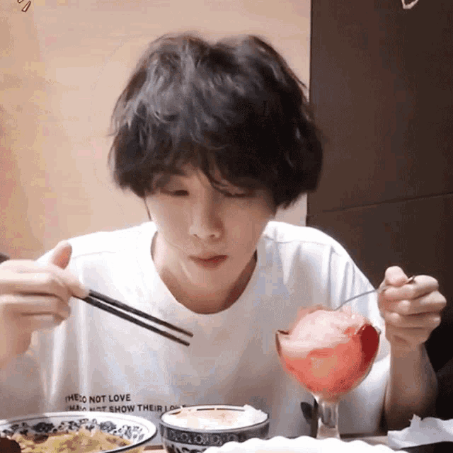 a person wearing a white shirt that says " i do not love " is eating food with chopsticks