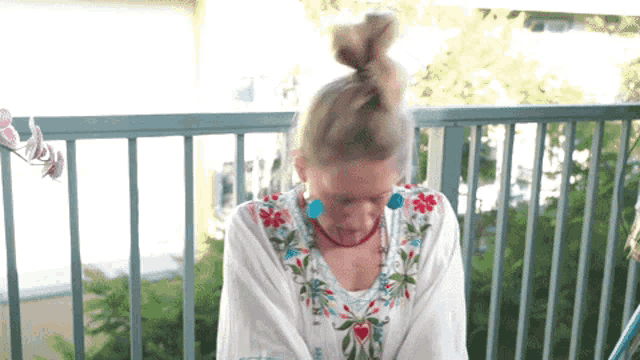 a woman is sitting on a balcony wearing a floral shirt