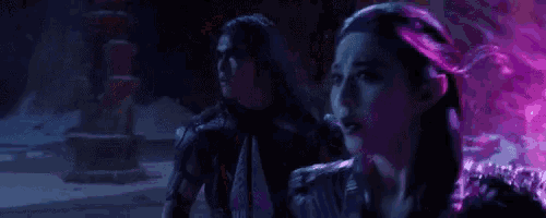a man and a woman are standing next to each other in a dark room with purple light coming out of the ceiling .