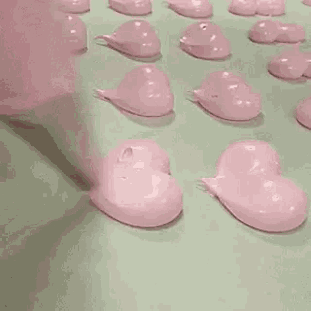 a person is spreading pink frosting in the shape of hearts on a green surface .