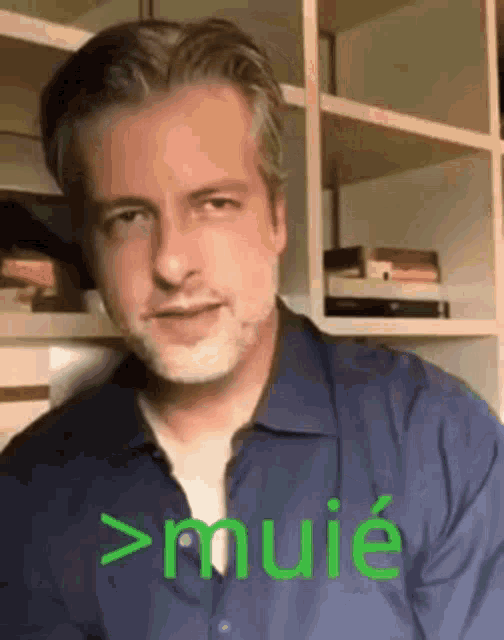 a man in a blue shirt is sitting in front of a bookshelf with the word muie written on it .