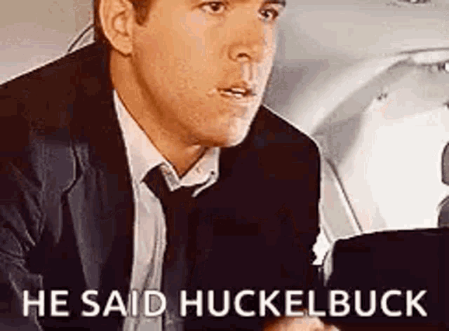 a man in a suit and tie is sitting in a car and saying he said huckelbuck .