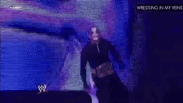 a man in a mask is standing in front of a large screen with the words wrestling in my veins on it .