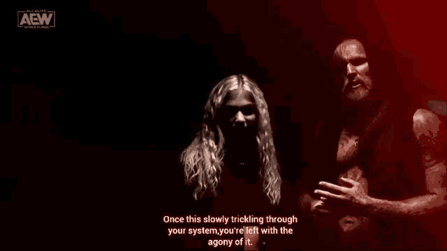 a man and a woman are standing next to each other in a dark room with a aew logo in the background .