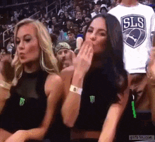 two women are sitting in the stands at a basketball game and one is wearing a sls shirt