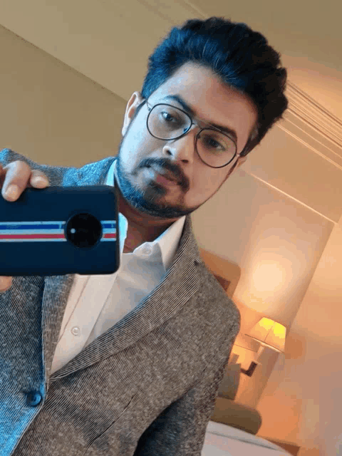 a man in a suit and glasses takes a selfie with his phone