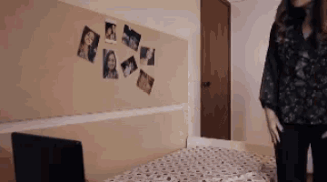 a woman is standing in front of a bed with pictures on the wall behind her