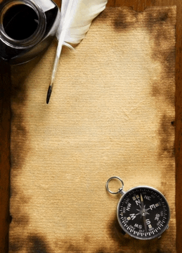 a compass is on a piece of paper next to a feather pen and ink bottle