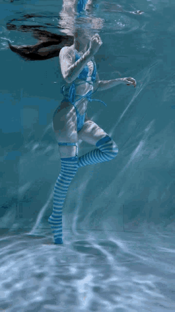 a woman in a bikini and striped thigh high socks is swimming underwater