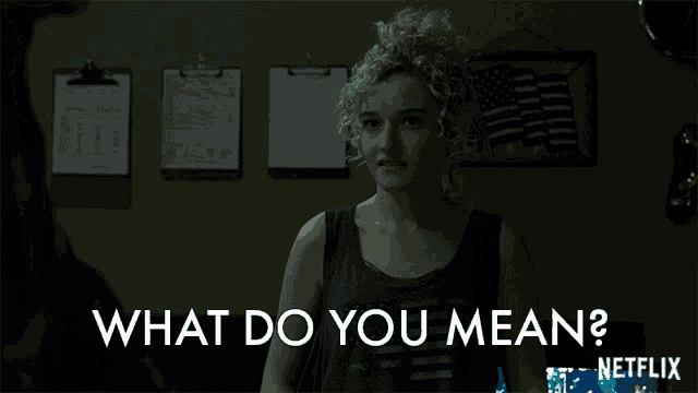 a woman with curly hair is standing in front of a wall that says what do you mean on it