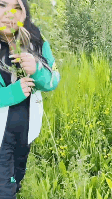 a woman is standing in a field of tall grass holding a plant in her hands .