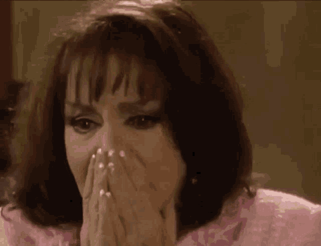 the woman is wearing a pink dress and covering her mouth with her hands .
