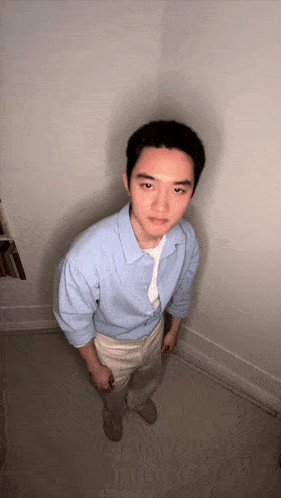 a man in a light blue shirt and khaki pants stands in a dark room