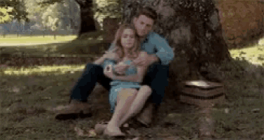 a man and a woman are sitting under a tree hugging each other .