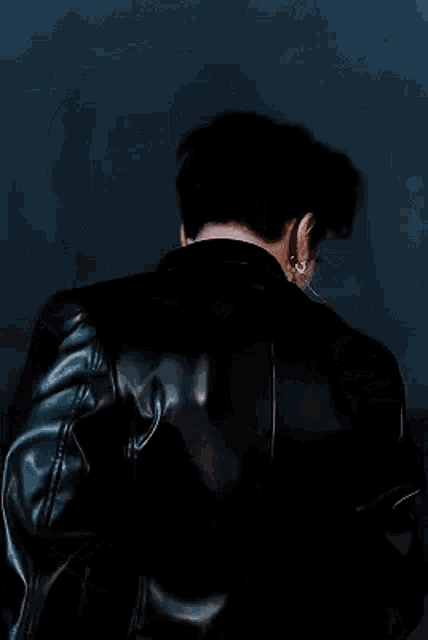 a close up of a young man wearing a black leather jacket and earrings .