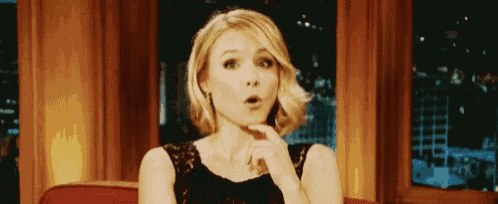 a woman in a black dress is making a surprised face with her hand on her chin .