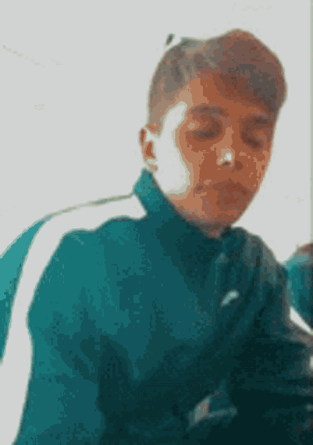 a young boy wearing a green jacket with white stripes is sitting in a chair .