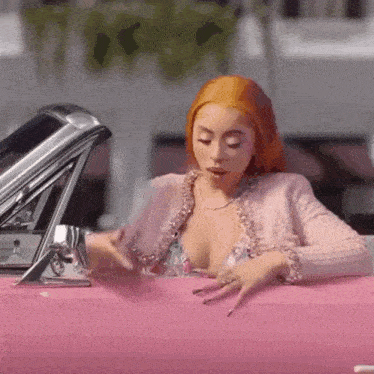 a woman with red hair is sitting in a pink car with her hands on the door .