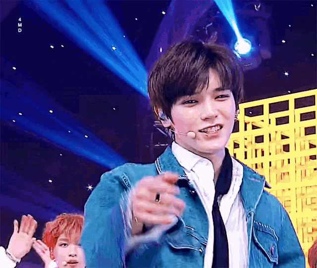 a young man wearing a blue jacket and tie is standing on a stage with a microphone .
