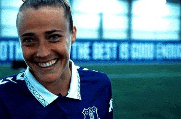 a woman in a blue shirt is smiling in front of a sign that says the best is good enough