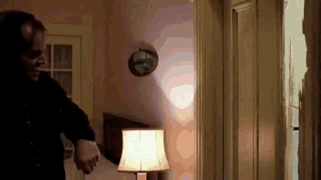 a man is standing in a room next to a lamp and a mirror .