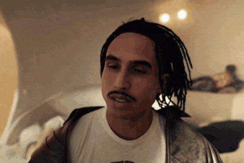 a man with dreadlocks and a mustache is wearing a white t-shirt