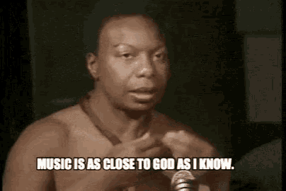 a man without a shirt is talking into a microphone and saying `` music is as close to god as i know . ''
