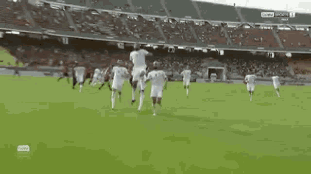 a group of soccer players are running on a field in front of a stadium .