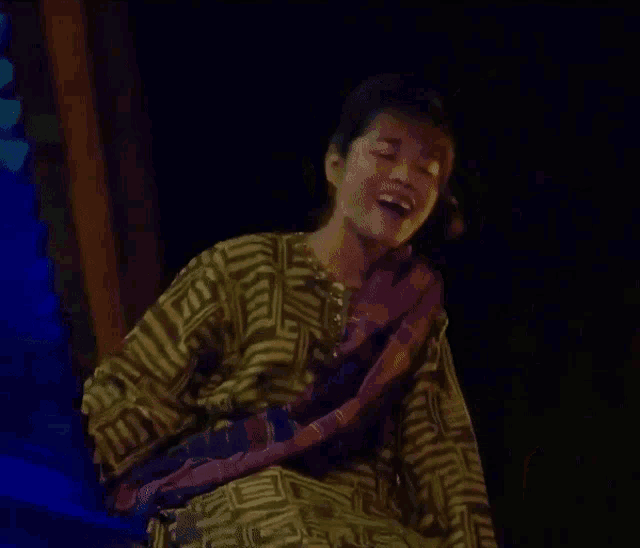 a woman in a yellow and purple striped shirt is sitting in the dark .