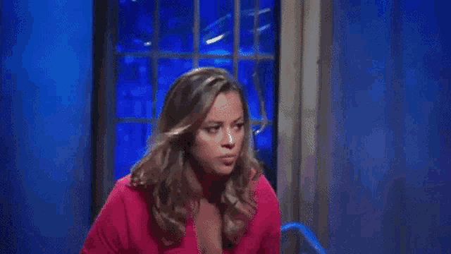 a woman in a pink shirt is standing on a stage in front of a blue curtain .