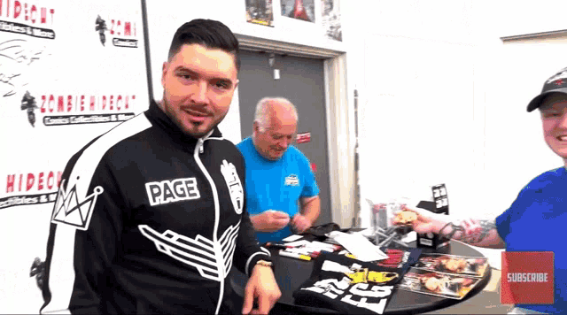a man wearing a jacket that says page stands in front of a table