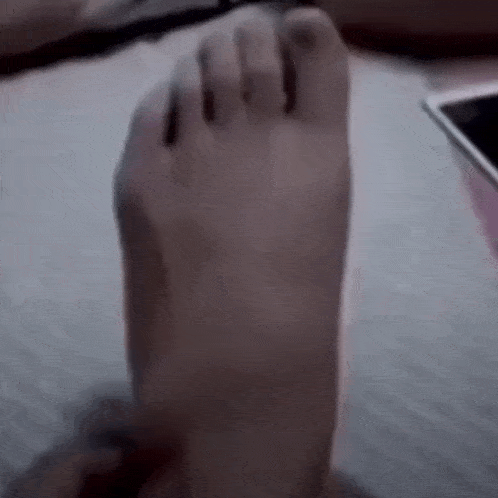 a person 's foot is laying on a bed next to a phone .