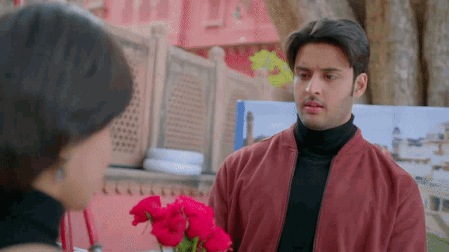 a man in a red jacket is holding a bouquet of red flowers