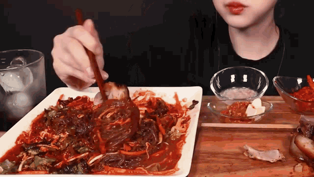 a woman eating a plate of food with chopsticks