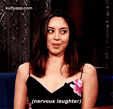 a woman in a black dress is smiling and saying `` nervous laughter '' while sitting on a couch .