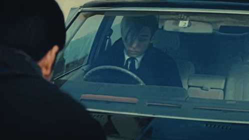 a man in a suit and tie is sitting in a car with a license plate that says 2