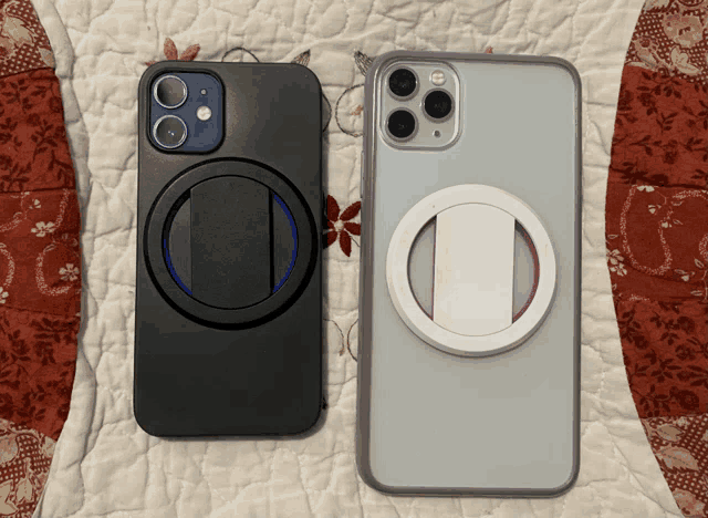 two cell phones are laying on a quilt with one having a blue lens